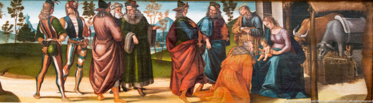 Richly dressed men approach the seated Virgin and Child, with one figure kneeling before the infant in a landscape setting.