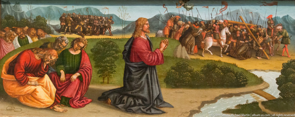 Robed figure kneels in prayer in a garden while companions rest nearby and armed soldiers approach in the distance.