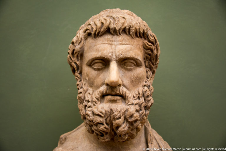 Marble bust of a young man with short curled hair, blank eyes, and a broad full beard.