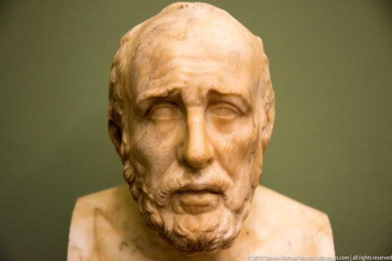 Marble portrait of an older balding man with sunken eyes, slightly open mouth, and short beard.