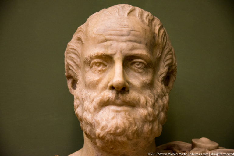 Frontal marble portrait of a mature bearded man with swept-back hair and deeply set eyes.