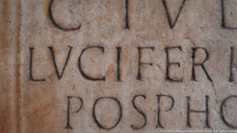 Close detail of weathered stone carved with large Latin capital letters, including the fragment LVCIFER.