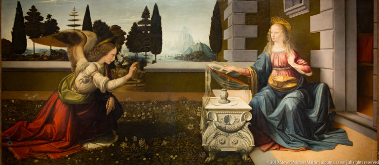 Leonardo’s Annunciation with Gabriel kneeling at left and Mary seated at an ornate lectern before a distant landscape.