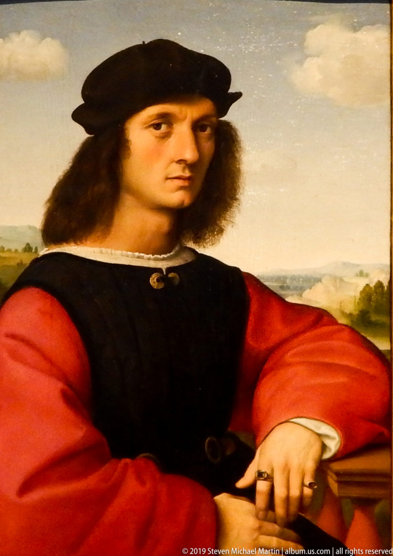 Young man in a black doublet, red sleeves, and dark cap sits with one hand resting on a book or ledge.
