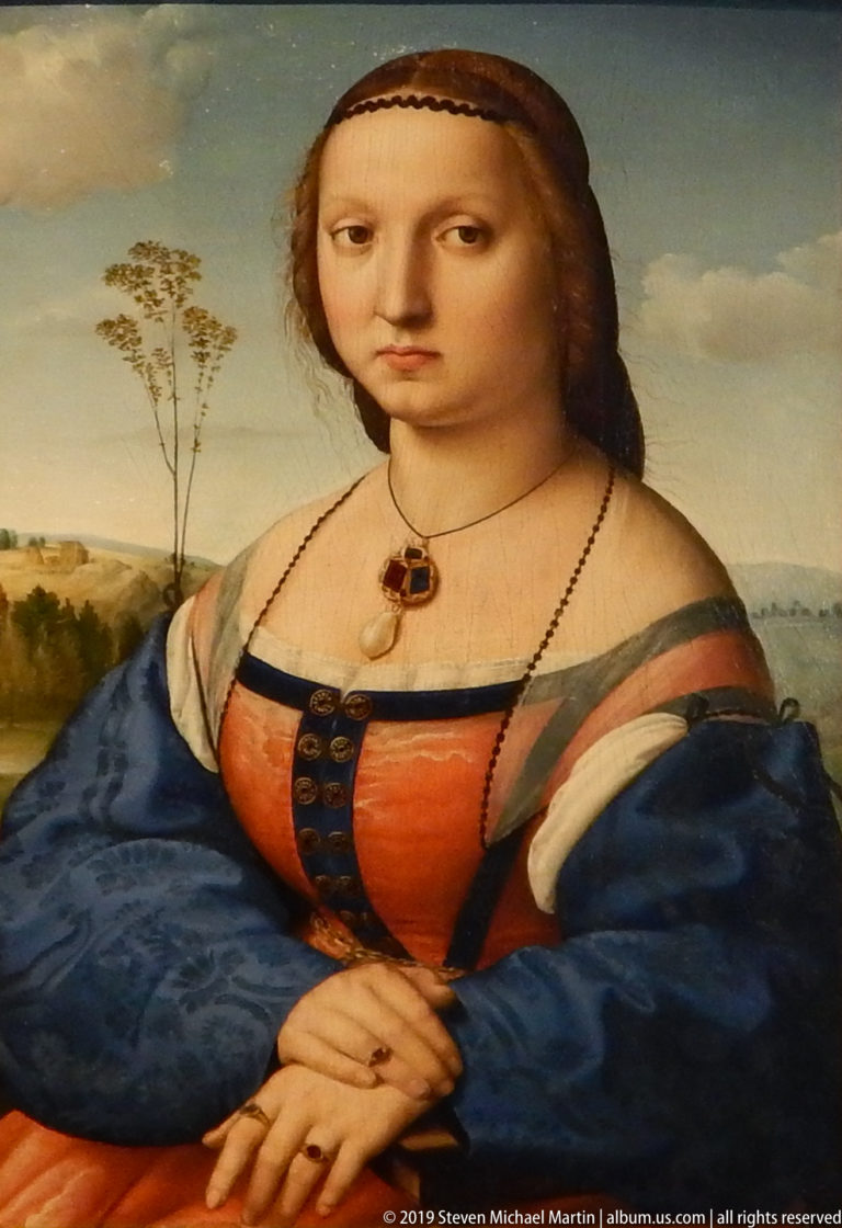 Young woman in a red bodice and blue sleeves sits with folded hands before a distant landscape.