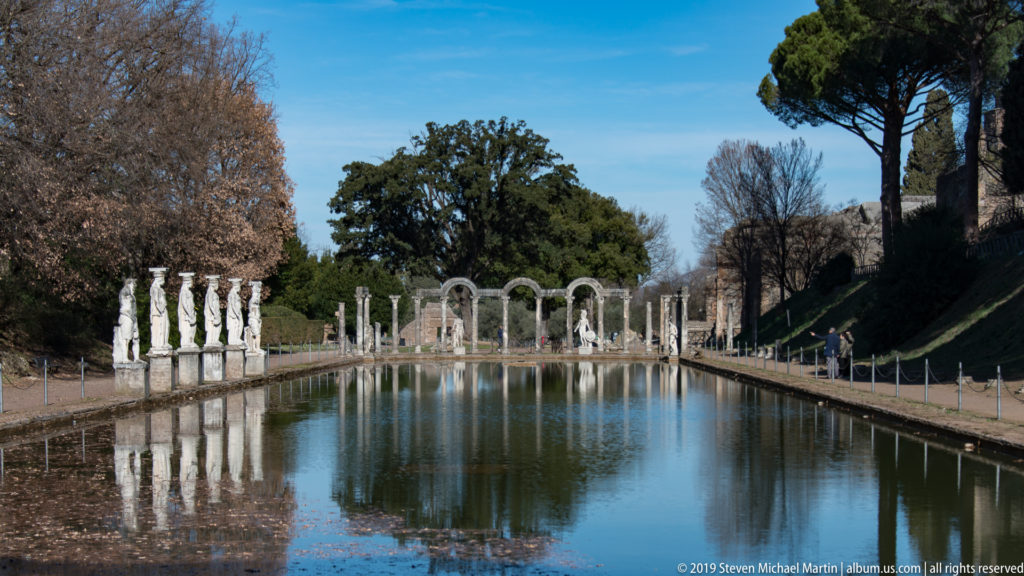 Long Canopus pool viewed on axis toward an arched colonnade, with caryatid statues lining the left bank.