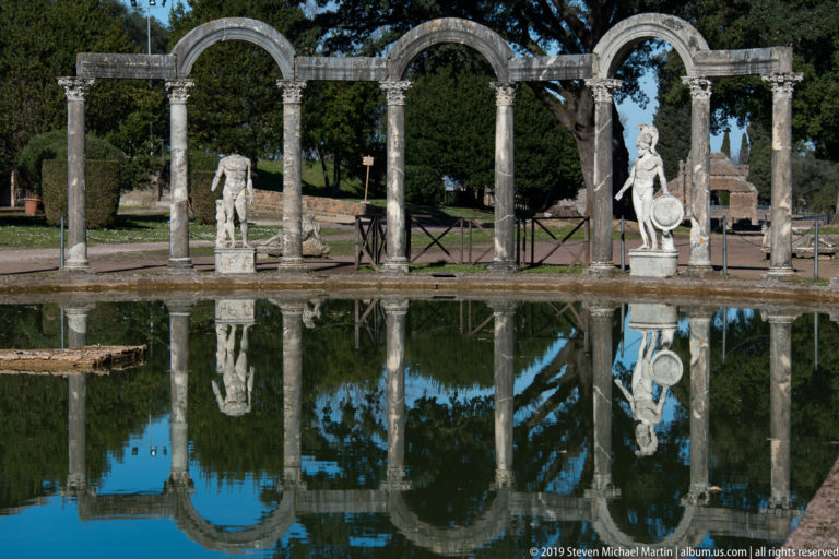Arched Canopus colonnade with statues at both ends and a near-complete reflection across the pool.