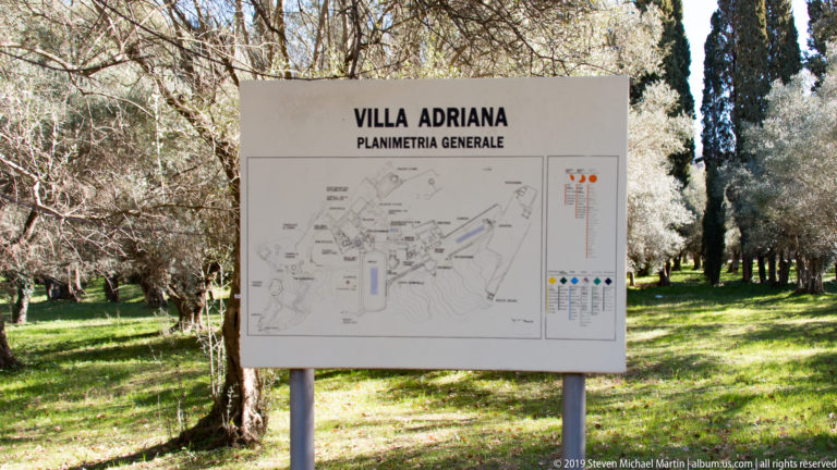 Outdoor sign reading “VILLA ADRIANA — PLANIMETRIA GENERALE” with a site map and legend, standing among trees.