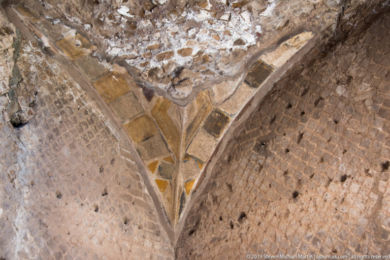 Triangular patch of ochre and cream geometric painted plaster surviving on a weathered masonry vault.