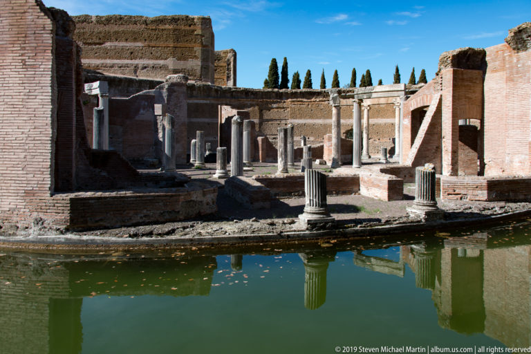 Short columns and brick room divisions of the Maritime Theatre central island reflected in green water.