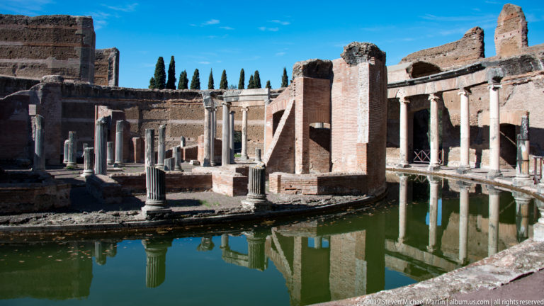 Brick walls and standing columns on the Maritime Theatre island reflected in the surrounding green water.