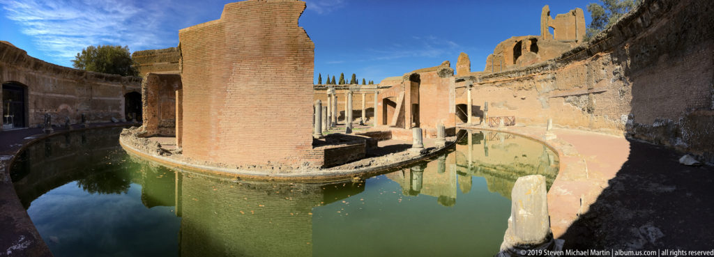 Curving green-water canal wraps around tall brick ruins on the central island of the Maritime Theatre.