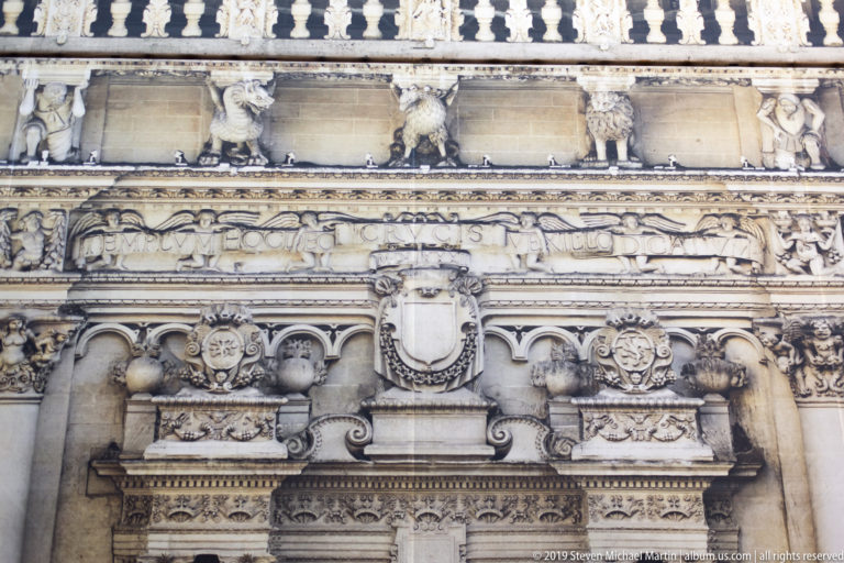 Close view of carved limestone columns, shields, floral reliefs and sculptural ornament above a historic doorway.