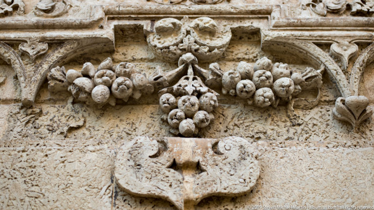 Weathered limestone relief carved with grape clusters, vine leaves and curling stems above a projecting stone element.