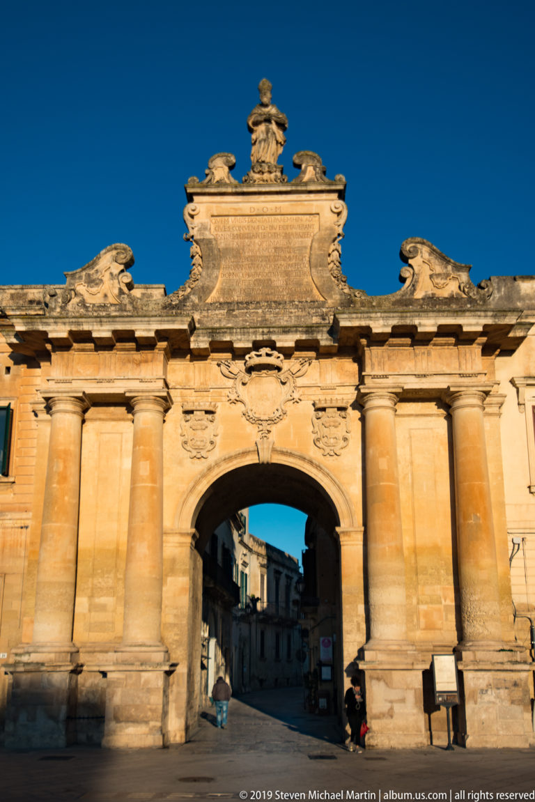 Close frontal view of Porta Napoli’s central arch, paired columns and sculpted upper masonry with a street visible beyond.