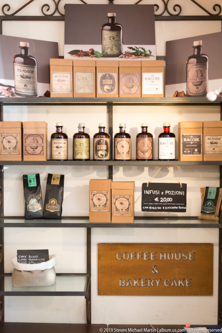 Shelves of boxed teas, tins and small jars above a wooden sign reading Coffee House Bakery Cake.