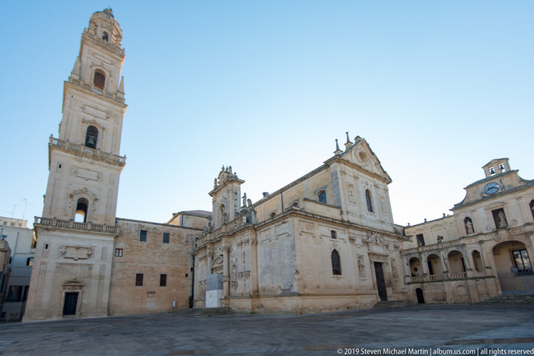 Broad Piazza del Duomo view with Lecce Cathedral, tall bell tower, ornate façades and open stone paving.