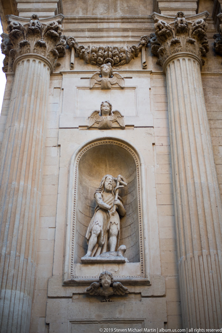 Carved religious figure in a recessed stone niche between large fluted columns, with garland ornament above.