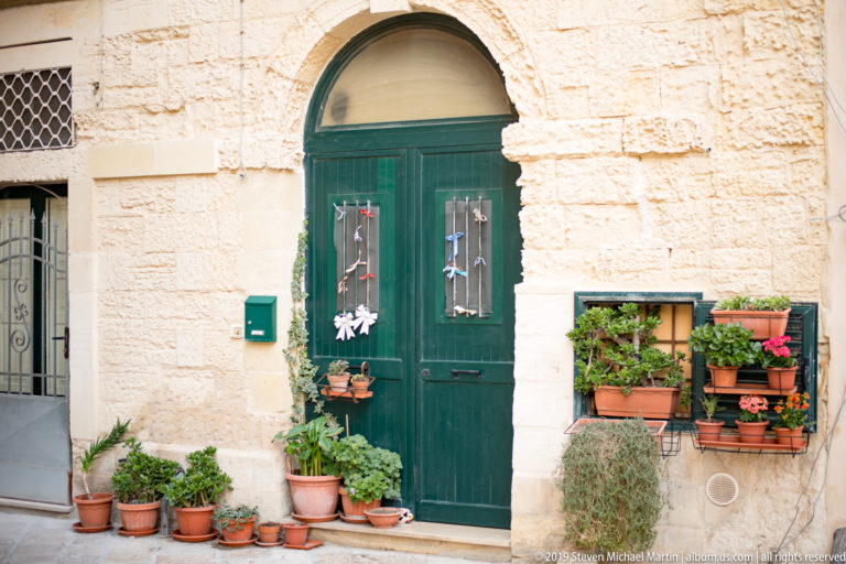 Dark green arched double door surrounded by terracotta pots and a matching green window box filled with plants.