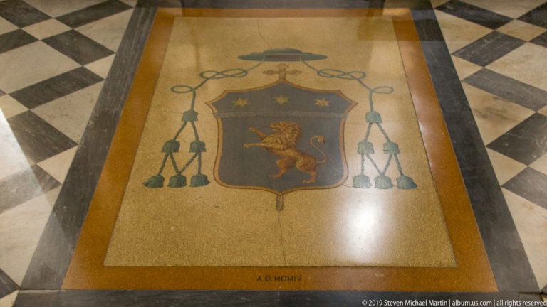 Floor inlay with Bishop Gennaro Trama’s blue coat of arms, three stars, rampant lion, episcopal hat and the date A.D. MCMIV.