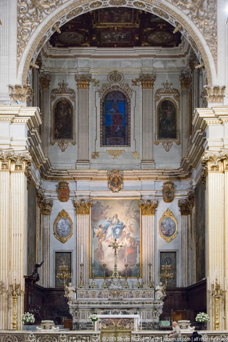 Lecce Cathedral presbytery with Oronzo Tiso’s Assumption above the marble high altar, flanked by gilded pilasters, paintings and walnut choir stalls.