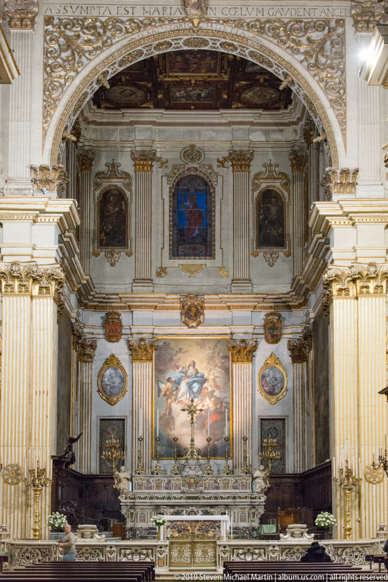 Presbytery centered on Oronzo Tiso’s 1757 Assumption of Mary, with oval saint paintings, gilded pilasters, marble altar and walnut choir stalls.