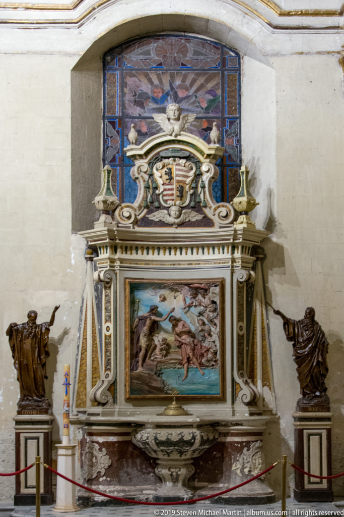 Lecce Cathedral baptistery with Raffaele Caretta’s Baptism of Christ relief, heraldic crest, basin, and statues of Moses and Ezekiel.