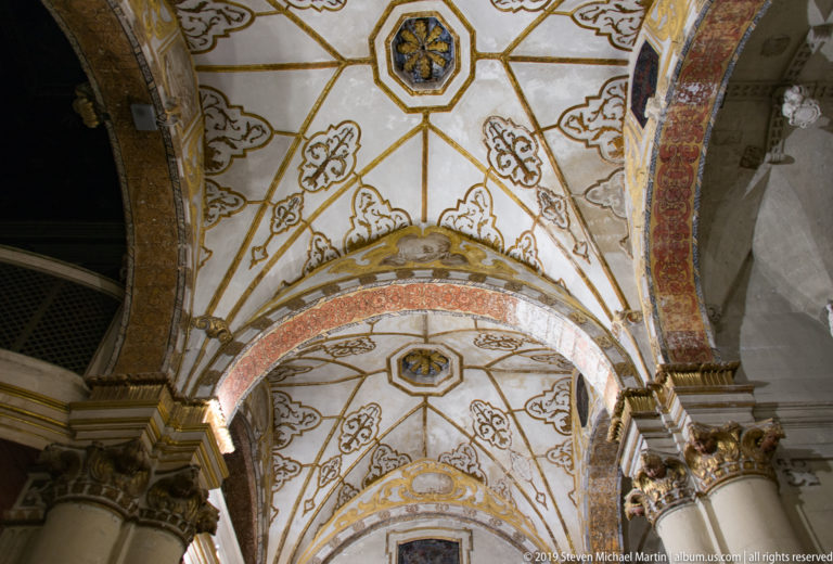 Oblique upward view along repeating white-and-gold vaults and decorated arches, with portions of stone columns below.