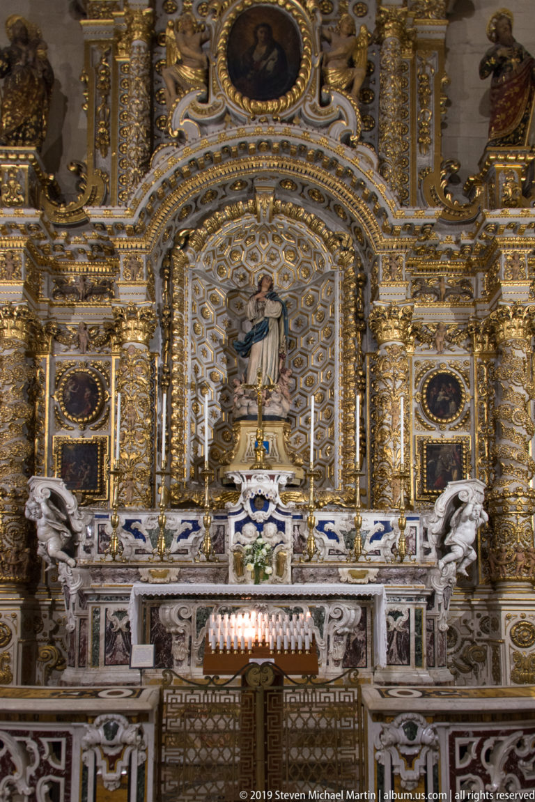 Highly gilded altar with a central statue of the Virgin Mary in a patterned niche, surrounded by portraits and sculptural ornament.