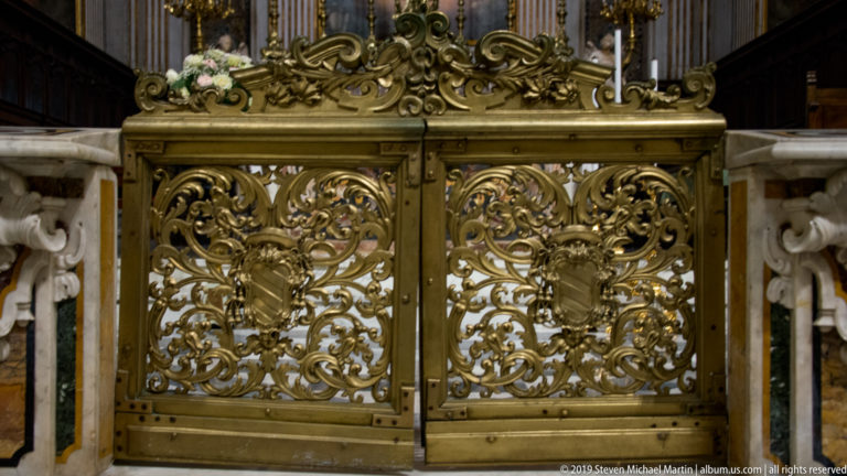 Close view of paired gilded metal altar gates filled with scrolling foliage and floral ornament.