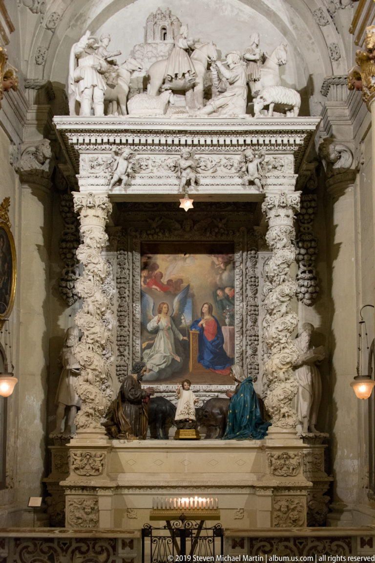 Large religious painting in an elaborate carved stone altar, with sculptural figures flanking the altar table below.
