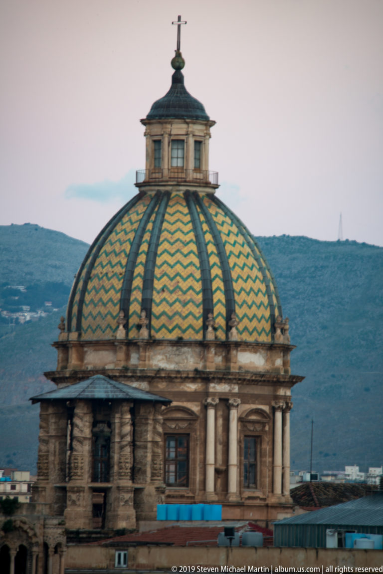 Turquoise and ochre geometric bands cover a ribbed dome beneath a small lantern and cross.