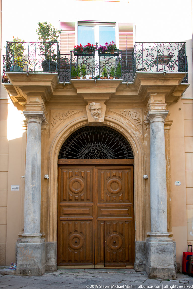 A carved stone portal frames double wooden doors beneath a balcony with flower boxes.