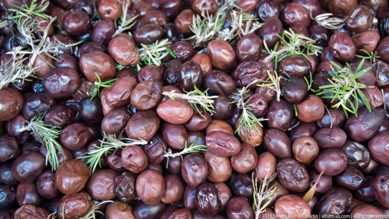 Dark purple olives and small green sprigs fill a close market display.