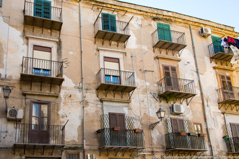 A tall Palermo façade has repeated balconies, shutters, small awnings and air-conditioning units.