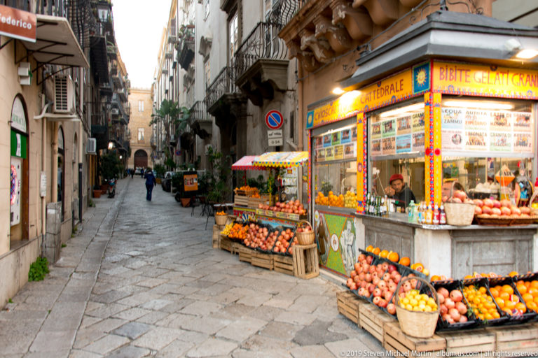Crates of oranges and produce line the sidewalk outside a brightly signed Palermo shop.