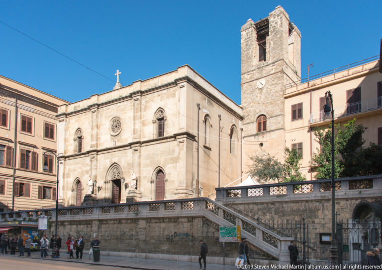 A pale church façade and separate arched bell tower face a paved square in Palermo.