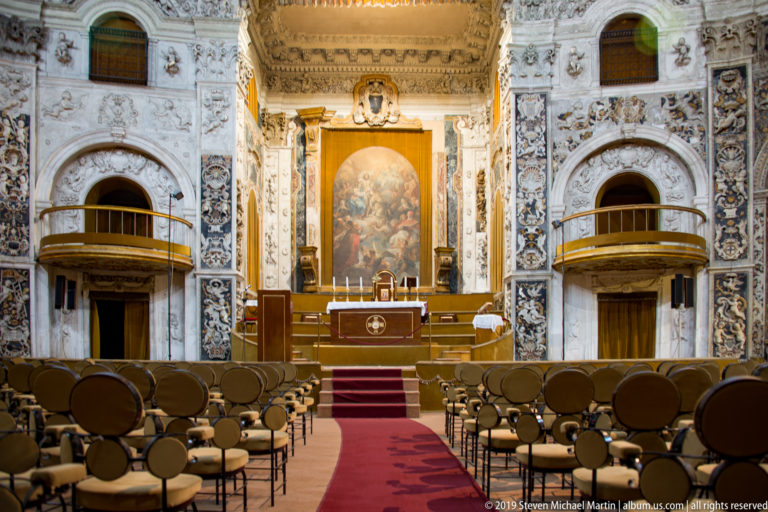 A red-carpeted aisle leads between pews toward a bright, ornate church altar.