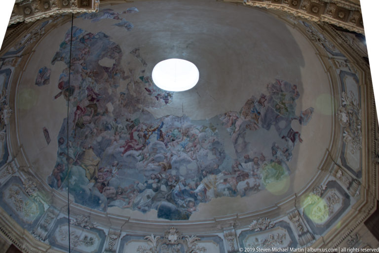 A large painted religious scene covers the vaulted ceiling above the church nave.