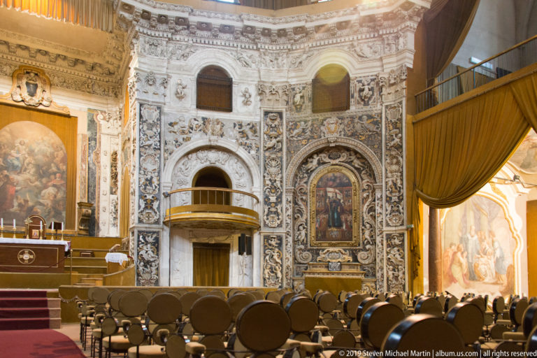 Rows of pews face an ornate Palermo church sanctuary with painted panels and gilded decoration.