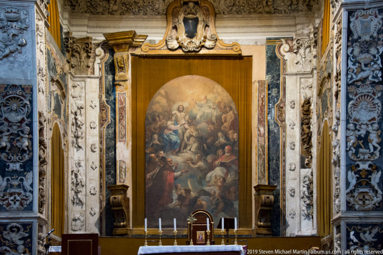 A central religious painting sits within a symmetrical carved surround in a Palermo church.