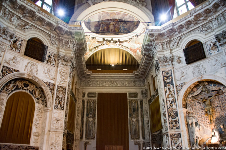 An ornate church arch and carved wall frames rise toward a bright opening in Palermo.