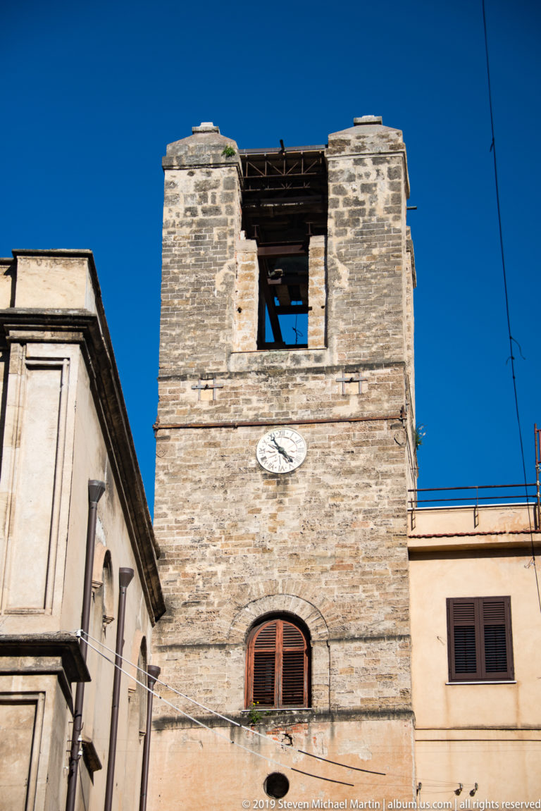 An upper bell tower with paired arches and a small clock rises above a Palermo roofline.