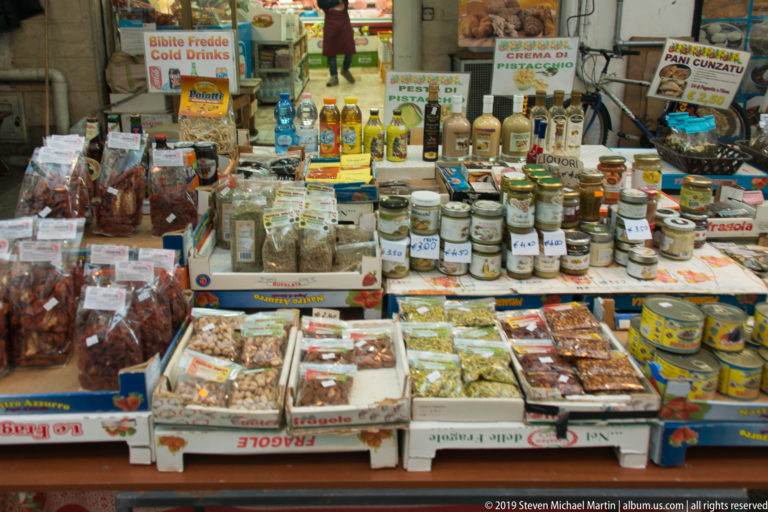 Bottles, tins and packaged foods crowd the shelves and counter of a Palermo shop.