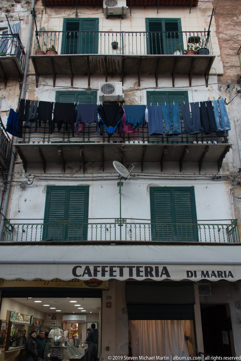 A blue awning marked Caffetteria di Maria projects beneath a balcony in Palermo.
