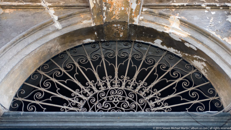 Curled wrought-iron scrollwork fills an arched opening above a doorway in Palermo.