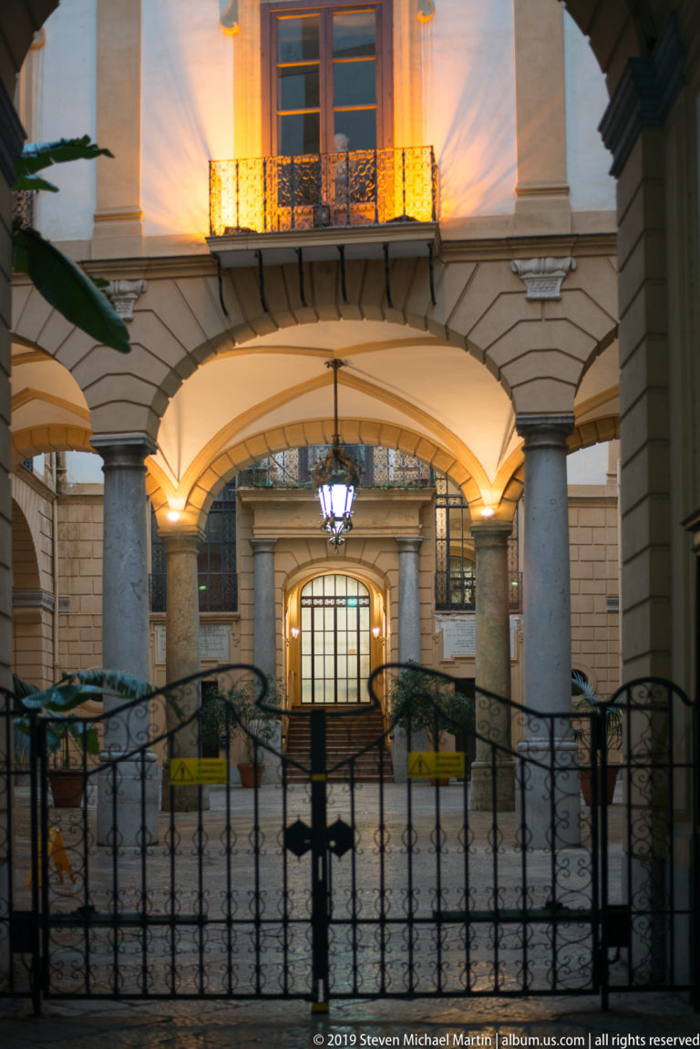 A lantern lights a gated stone entrance beneath a balcony in Palermo.