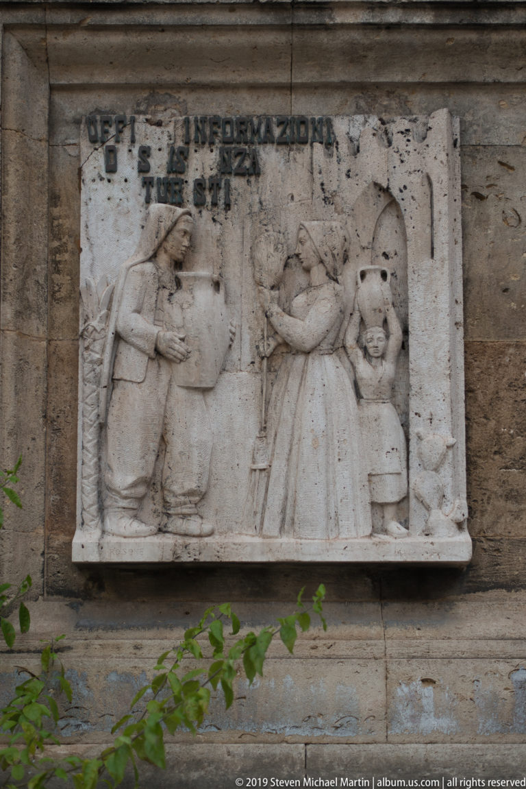 An angled interpretive panel shows an illustrated sculptural group and text about Palermo heritage.
