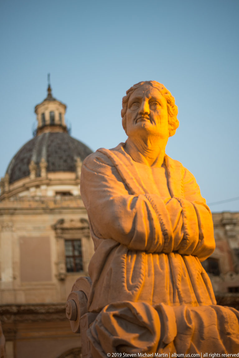 A close upward view of a carved male figure at Fontana Pretoria with a dome behind.