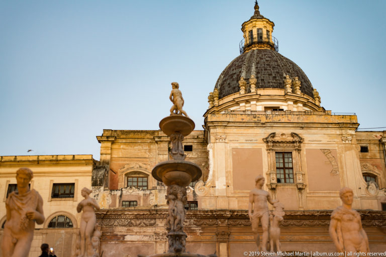 Statues of Fontana Pretoria stand before the red dome and pale façade of San Cataldo.
